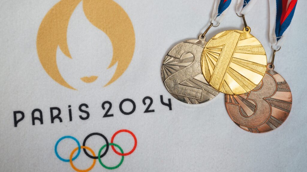 Close-up image of the gold, silver, and bronze medals for the Paris 2024 Olympics placed on the official Paris 2024 logo background. Showcasing the Olympic spirit and the prestigious awards for athletic excellence, this image highlights the intricate design of the medals and the iconic Olympic rings.