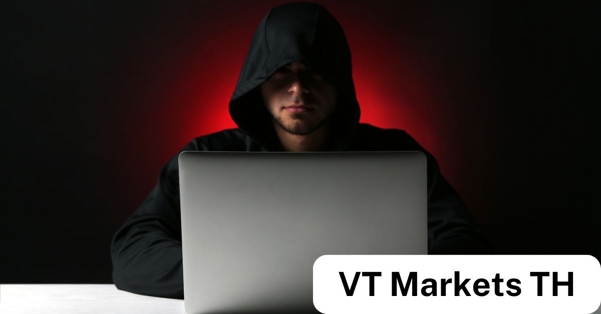 A person wearing a dark hoodie sits in a dimly lit room, illuminated by a glowing laptop screen, symbolizing the dangers of online Forex scams in Thailand.