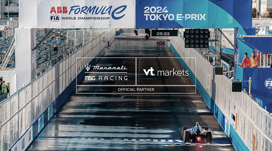 The Maserati MSG Racing car speeds along the track at the 2024 Tokyo E-Prix, under the banner of the ABB FIA Formula E World Championship. Prominent advertising for VT Markets, an official partner, is displayed alongside other sponsors. The event showcases electric racing technology in a vibrant, urban setting.