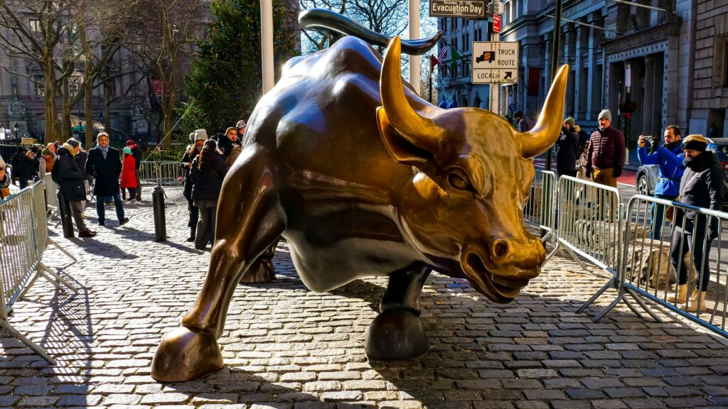 Charging Bull sculpture in Wall Street, New York, surrounded by tourists with a clear winter sky, symbolising bullish market trends in trading